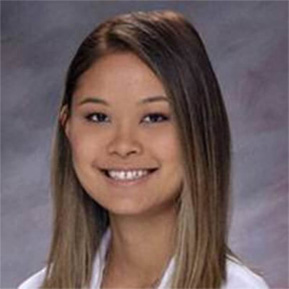 The image shows a young woman with a smile, posing for a portrait. She has long hair and is wearing a white shirt. Her attire suggests she could be a student or an employee at an educational institution.