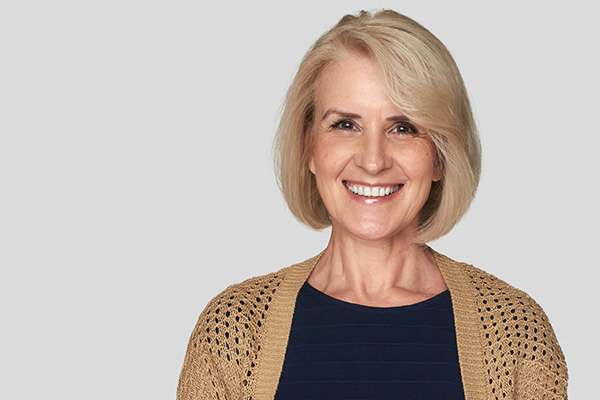 A woman with blonde hair smiling at the camera, wearing a blue top and a beige cardigan.