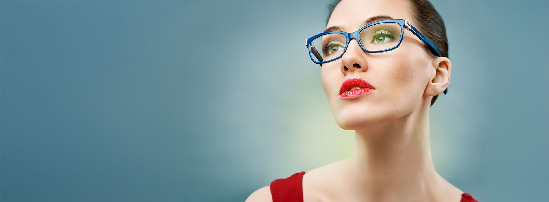 The image features a woman with glasses, wearing a red top, standing against a blue background with a light source creating a halo effect around her head.