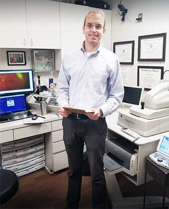 Man standing in front of an office desk with a laptop, holding a tablet with both hands.