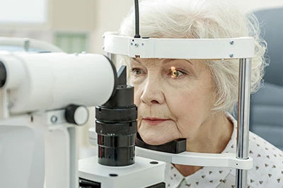 An older woman using an eye exam machine, likely at an optician s office.