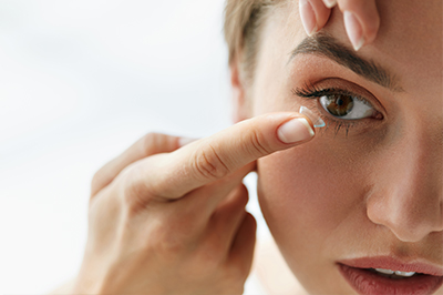 The image shows a close-up view of a person applying makeup around their eyes using a small brush, with a focus on precision and care.