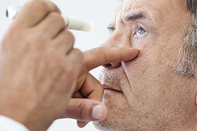 An elderly man receiving medical attention with a professional holding an eye dropper over his eye.